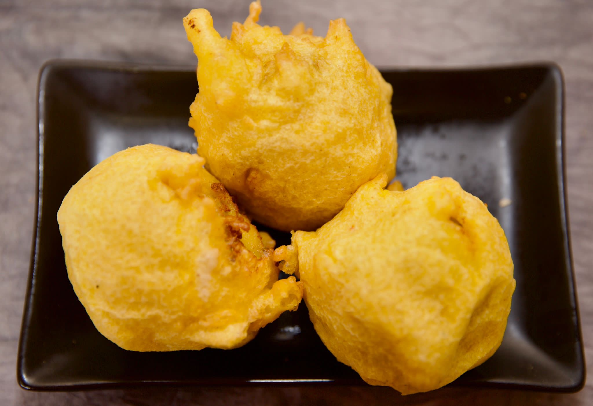 Three golden fried bonda on a black plate