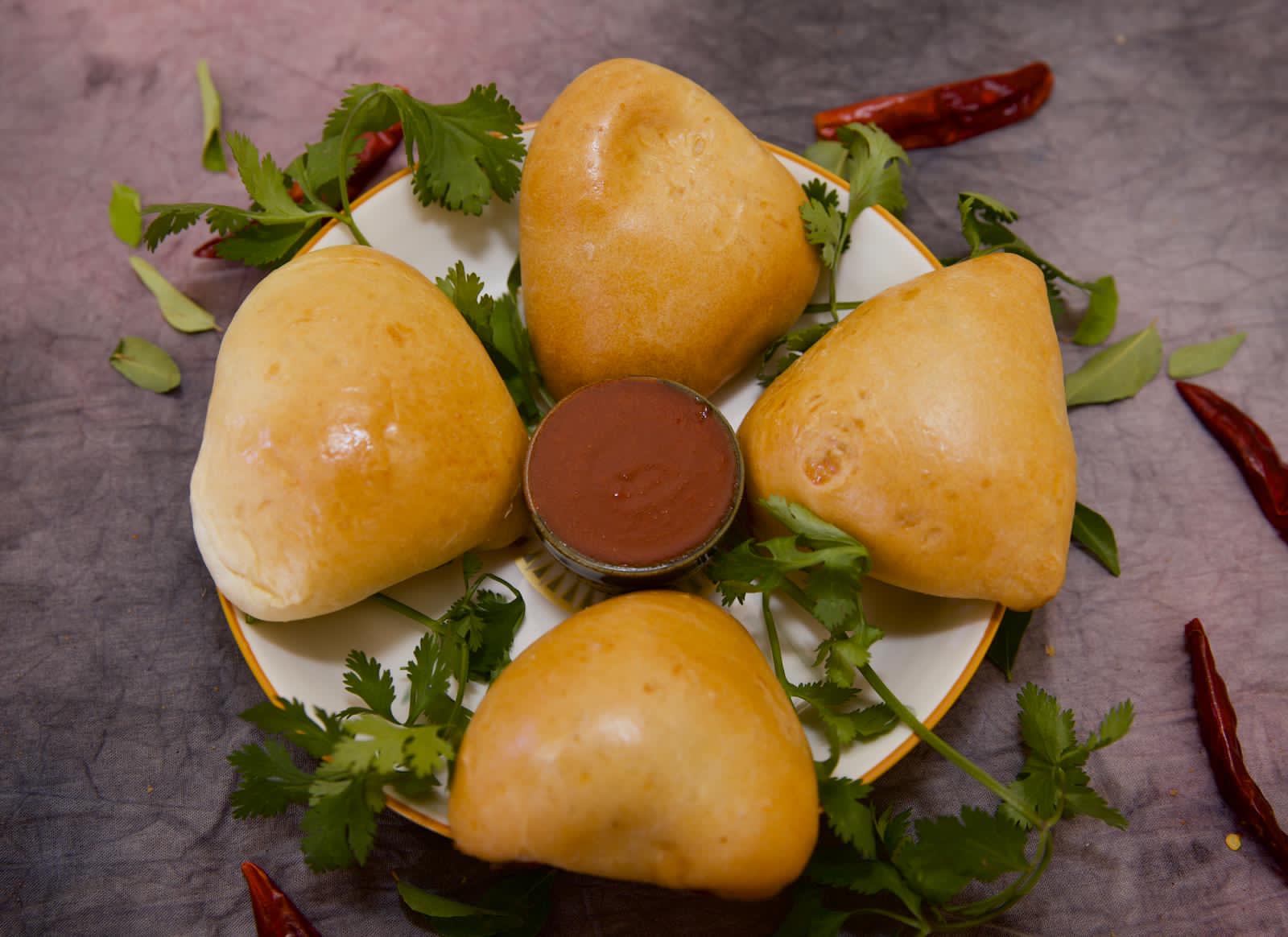 Four glazed bakery buns around a bowl of spiced dipping sauce
