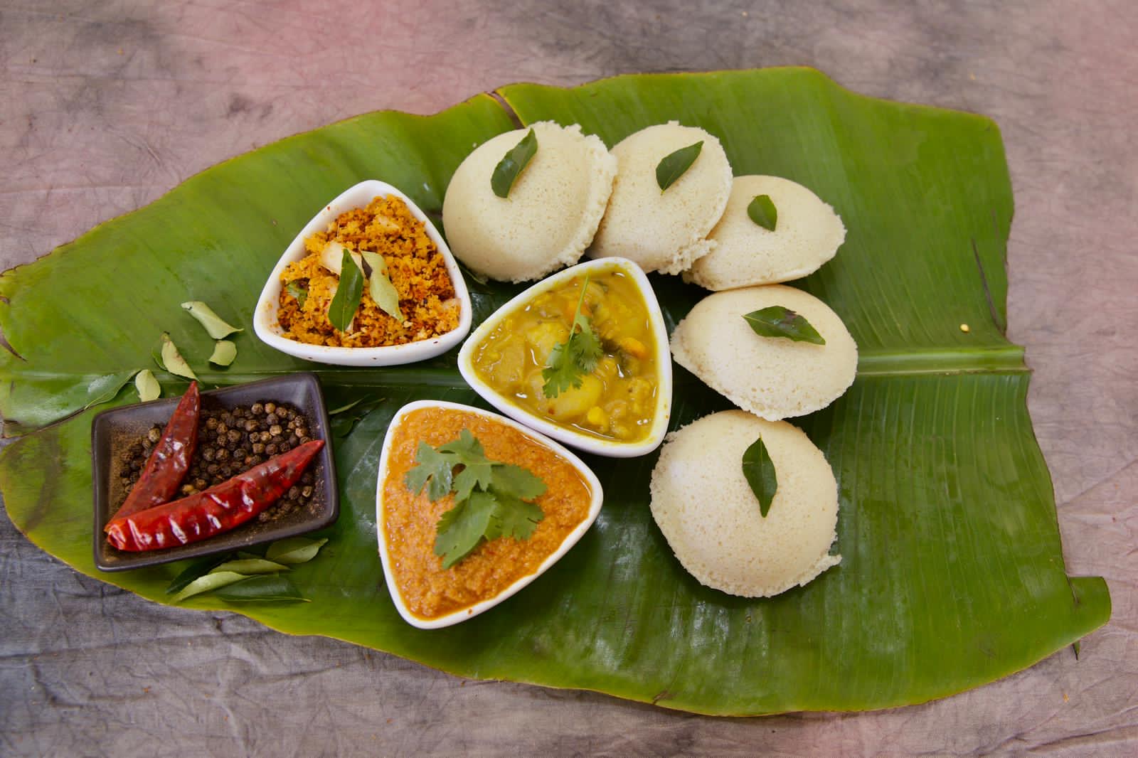Four steamed idli on a banana leaf with coconut chutney, sambal and potato curry