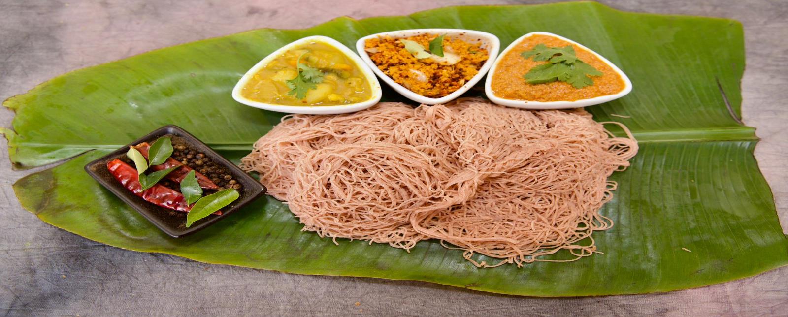 Red rice string hoppers on a banana leaf with chutney, sambal and potato curry